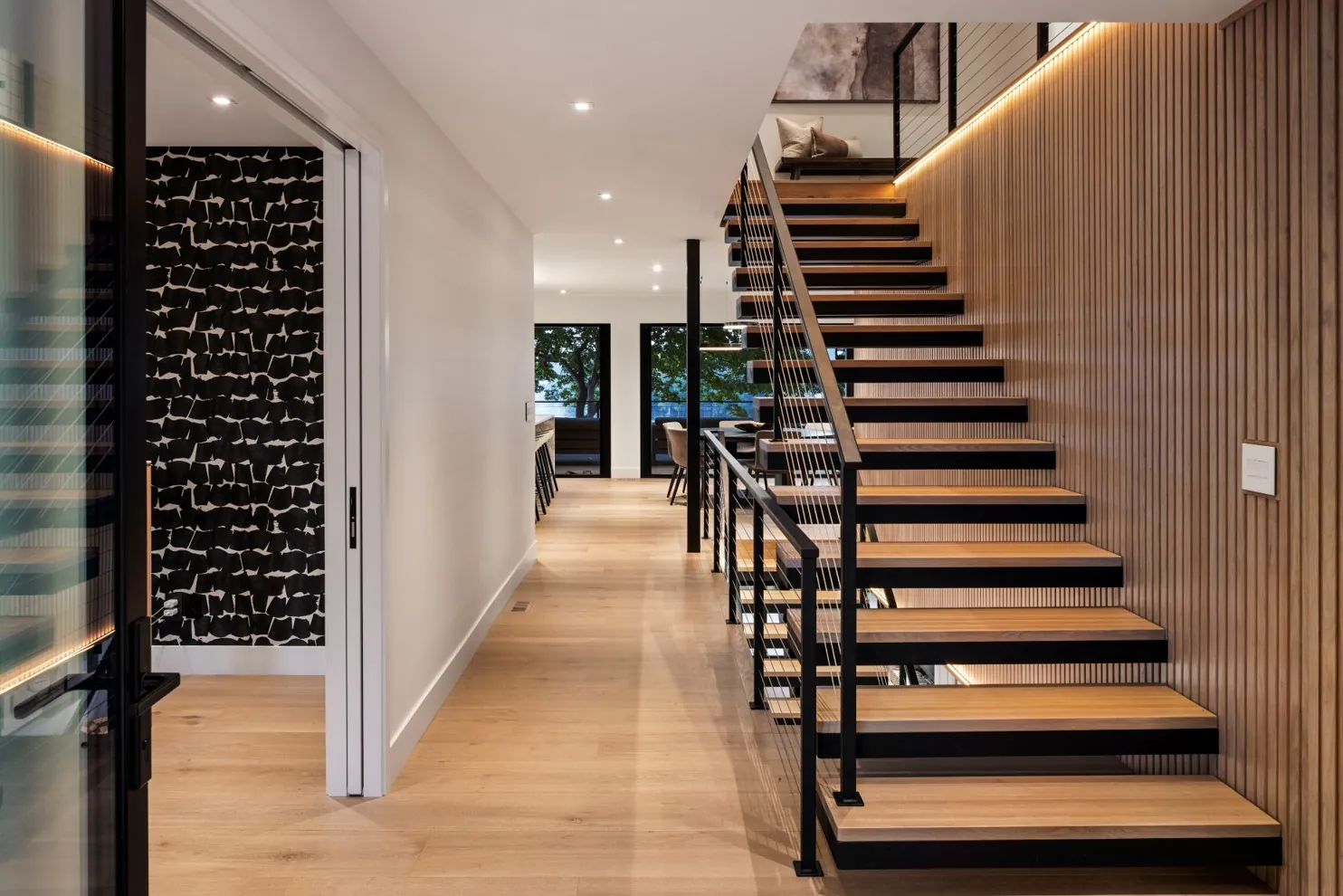 Oak staircase with a black steel railing beside a wide-plank floor